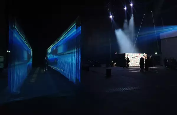 54: Manchester's installation in the warehouse – showing a fabric walkway with a film projected on to it and an enclosed, collaged box with performers inside