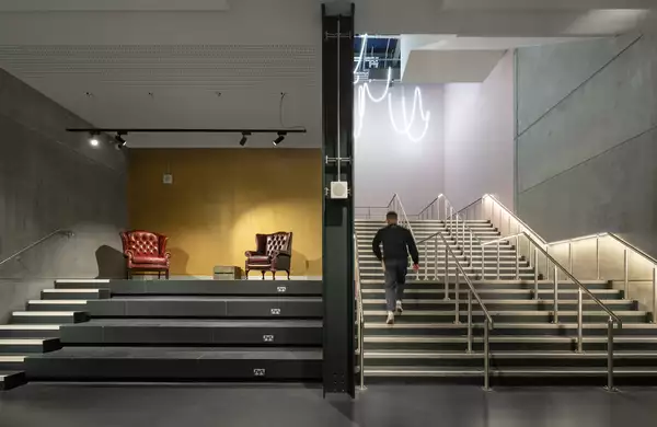 A visitor walking up the Warehouse staircase next to a stage with two armchairs on