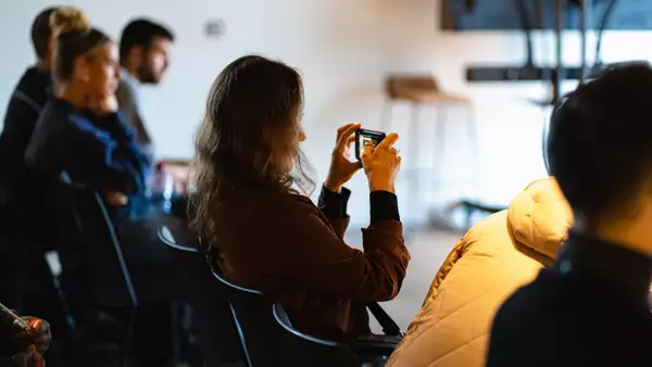 Audience member taking a photo with a smartphone during a panel discussion. The background is blurry.