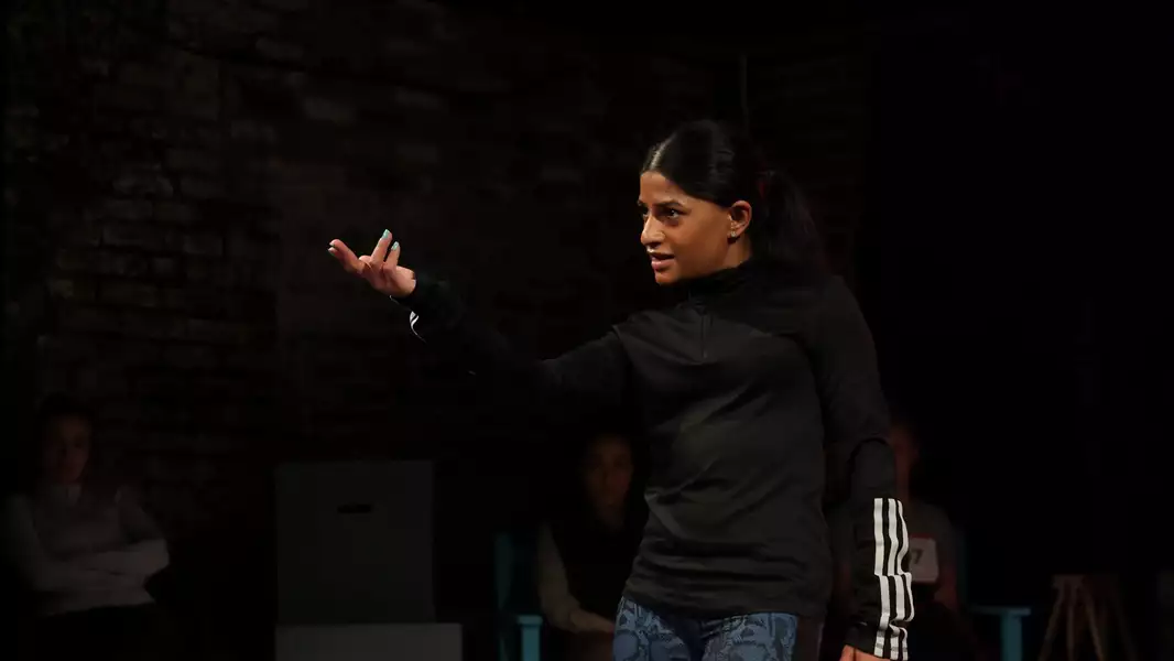 Haiesha Mistry wearing all black, with her fingers stretched out in front of her, beckoning to somebody off camera