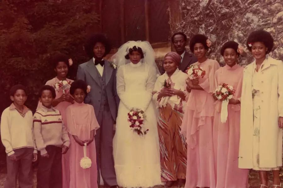 Family photograph on a wedding day. The bride is wearing white and standing in the middle of the photo. The men are wearing suits and the bridesmaids are wearing light pink. The photo is sepia-toned.