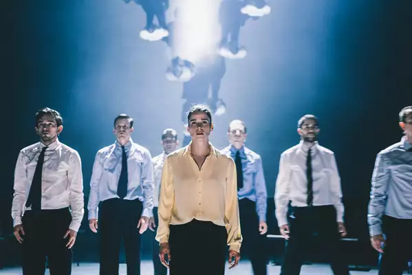 A still from Figures in Extinction [2.0] showing seven performers stood upright, wearing suits and staring at the audience