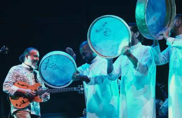 Four members of Ghazi & Boom.Diwan X Arturo O'Farrill performing on stage wearing white robes