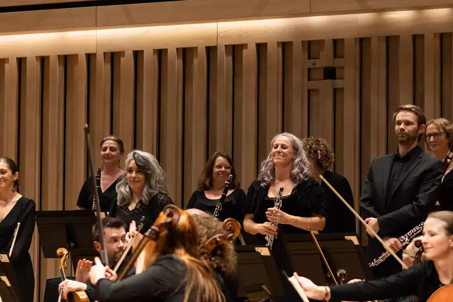 The woodwind section of Manchester Camerata standing up on stage and smiling