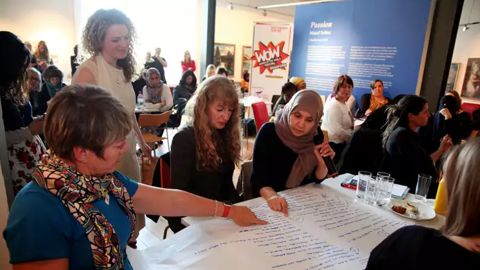 A group of people writing on and pointing at a large piece of paper