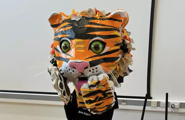 A child wearing a giant tiger puppet on their head