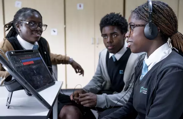 Three children sat around an iPad, one wearing headphones
