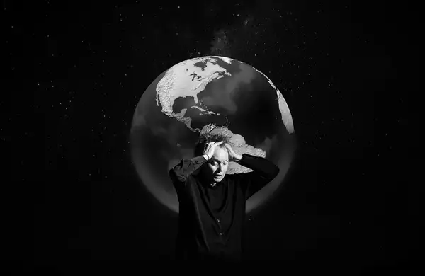 Black and white image of Laurie Anderson with her eyes closed and hands on her hand. Behind her is the earth.