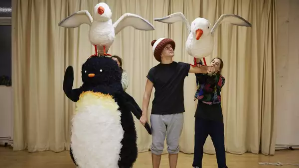 Adult size penguin costume and actor in giant bobble hat with a puppet penguin on his arm
