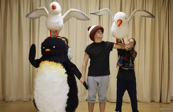 Adult size penguin costume and actor in giant bobble hat with a puppet penguin on his arm