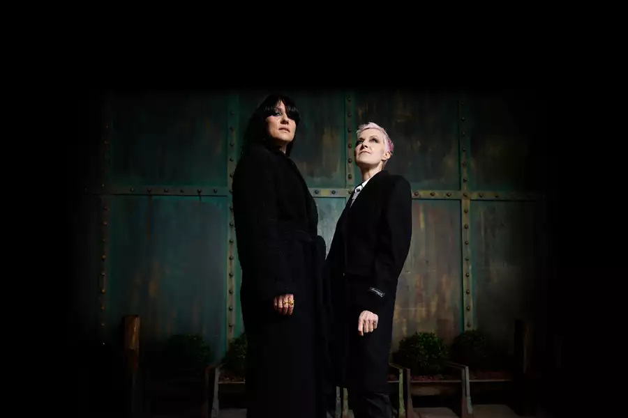 Anna Phoebe and Mary Anne Hobbs dressed in black stand against a rustic metal background, looking upwards.