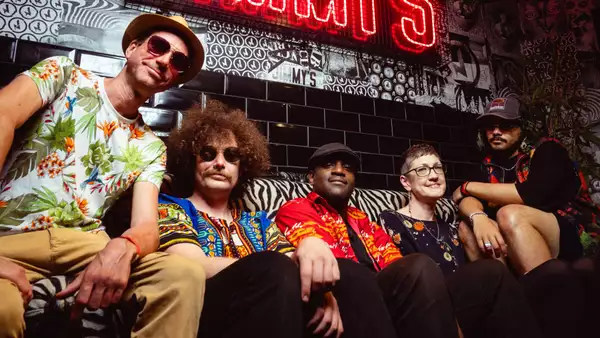 band NGUVU sit on a sofa in a bar smiling with a neon sign behind them