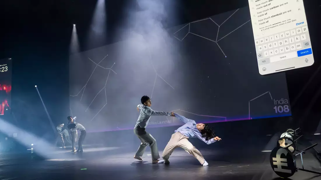 A performance of The Accountants showing six dancers centre stage – with two giant phone screens either side of the stage