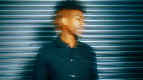 artist Obeka standing in front of a metal corrugated shutter looking wistfully to the side