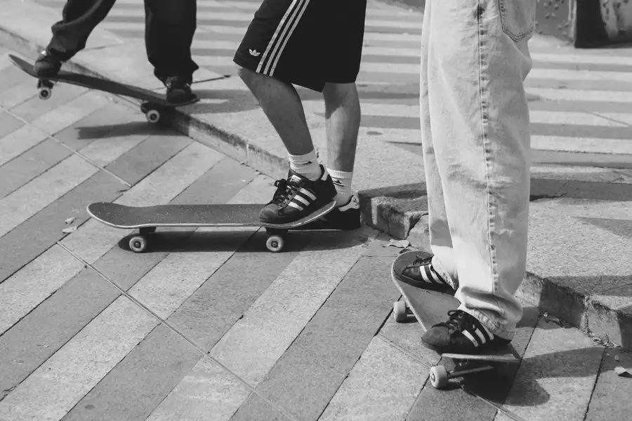 Black and white photograph of three people's feet on skateboards wearing adidas trainers