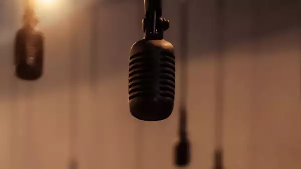 A close-up of a microphone hanging from above, with several similar microphones blurred in the background. The warm lighting and soft focus create an atmospheric feel.