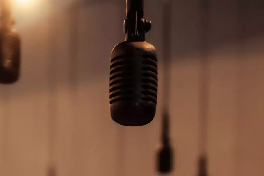 A close-up of a microphone hanging from above, with several similar microphones blurred in the background. The warm lighting and soft focus create an atmospheric feel.