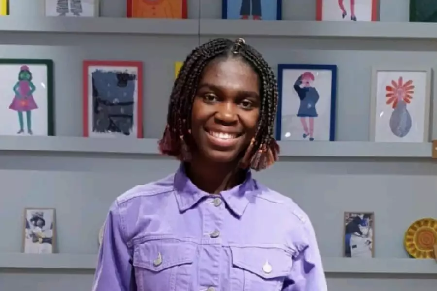 Photo of Ibukun smiling wearing a purple top and standing in front of some prints