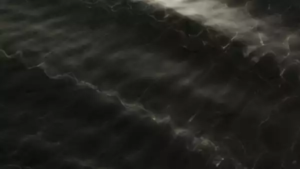 This image shows a dark, wavy surface with subtle reflections, resembling the texture of water ripples or light passing through water.