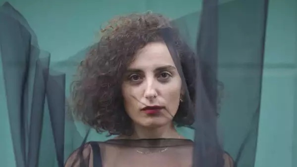 Sanem Kalfa stood in front of a turquoise wall, with a black transparent piece of material covering her face