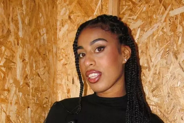 Victoria Jane wearing a black top, stood in front of a MDF wood background
