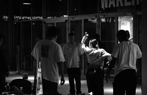 A black and white photograph of a group of people in the Social, which is dimly lit. One person is energetically dancing while others watch.